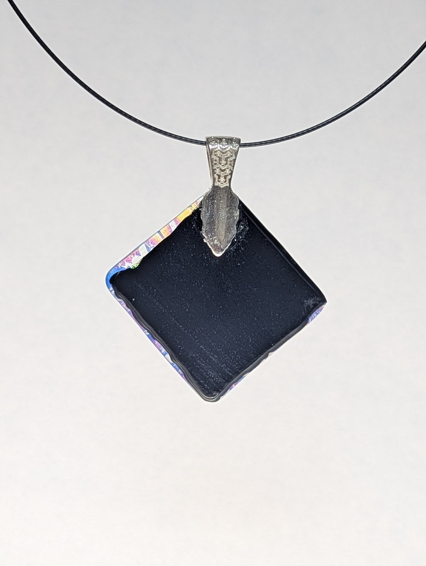 The black back of a blue dichroic fused glass pendant with a silver metallic clasp, displayed on a black stainless steel necklace.