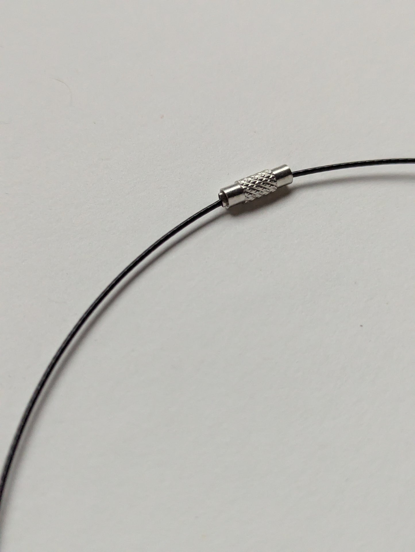 Close-up of a black stainless steel necklace with a screw clasp on a plain background.