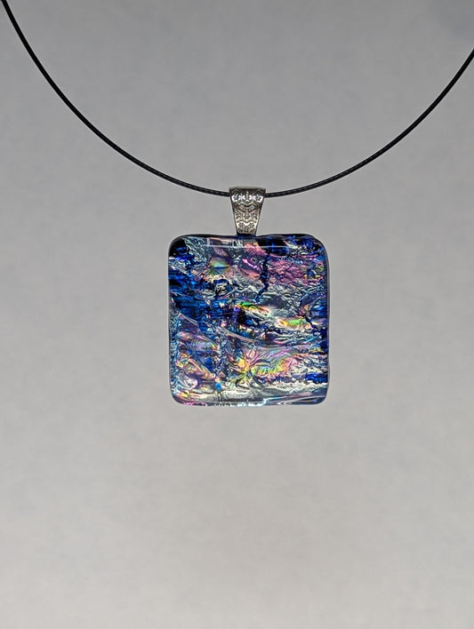 A blue and silver iridescent fused glass pendant with a metallic clasp, displayed on a black stainless steel necklace against a white background.