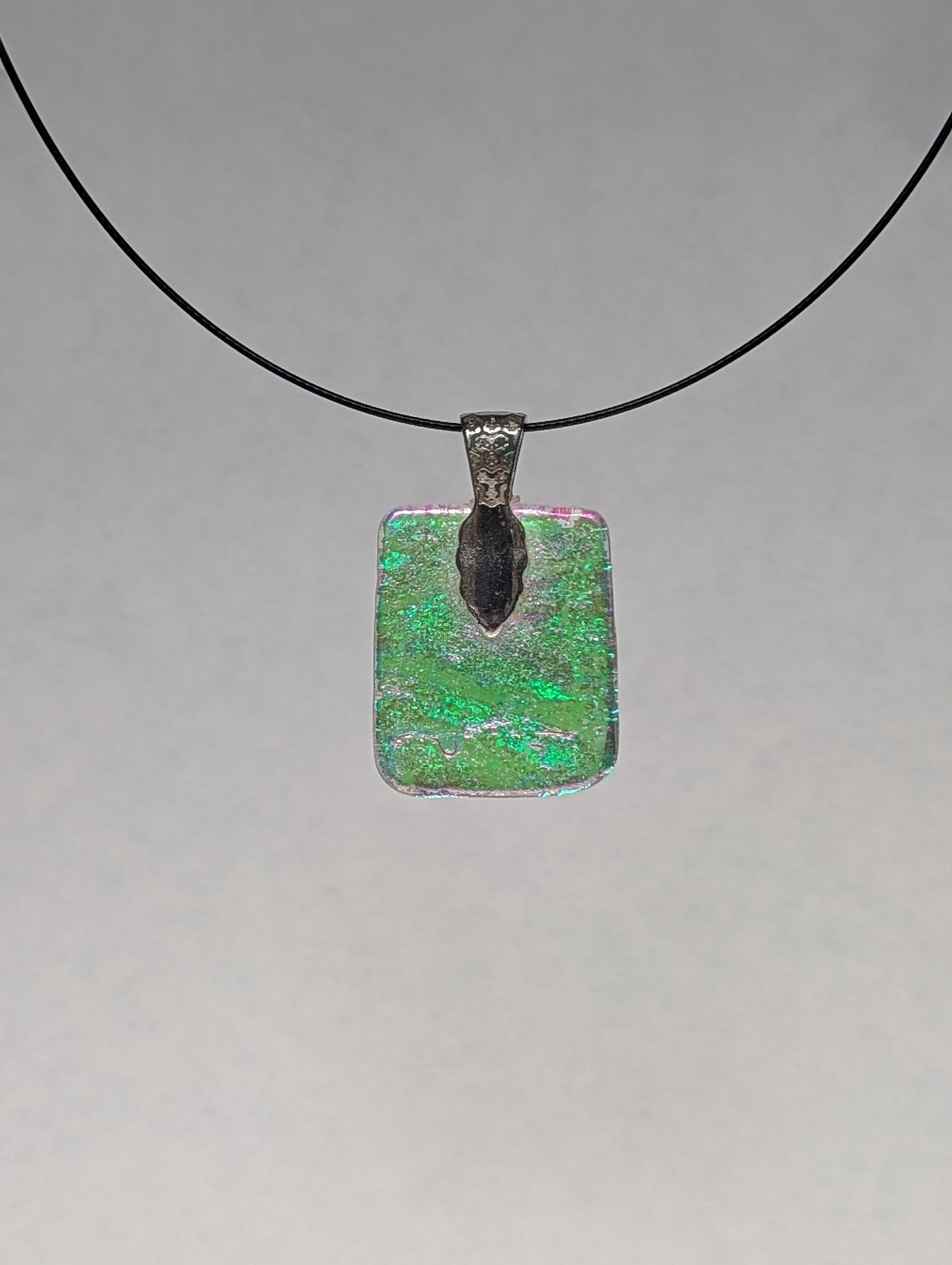 The back of a colorful clear dichroic fused glass pendant with a silver metallic clasp, displayed on a black stainless steel necklace.