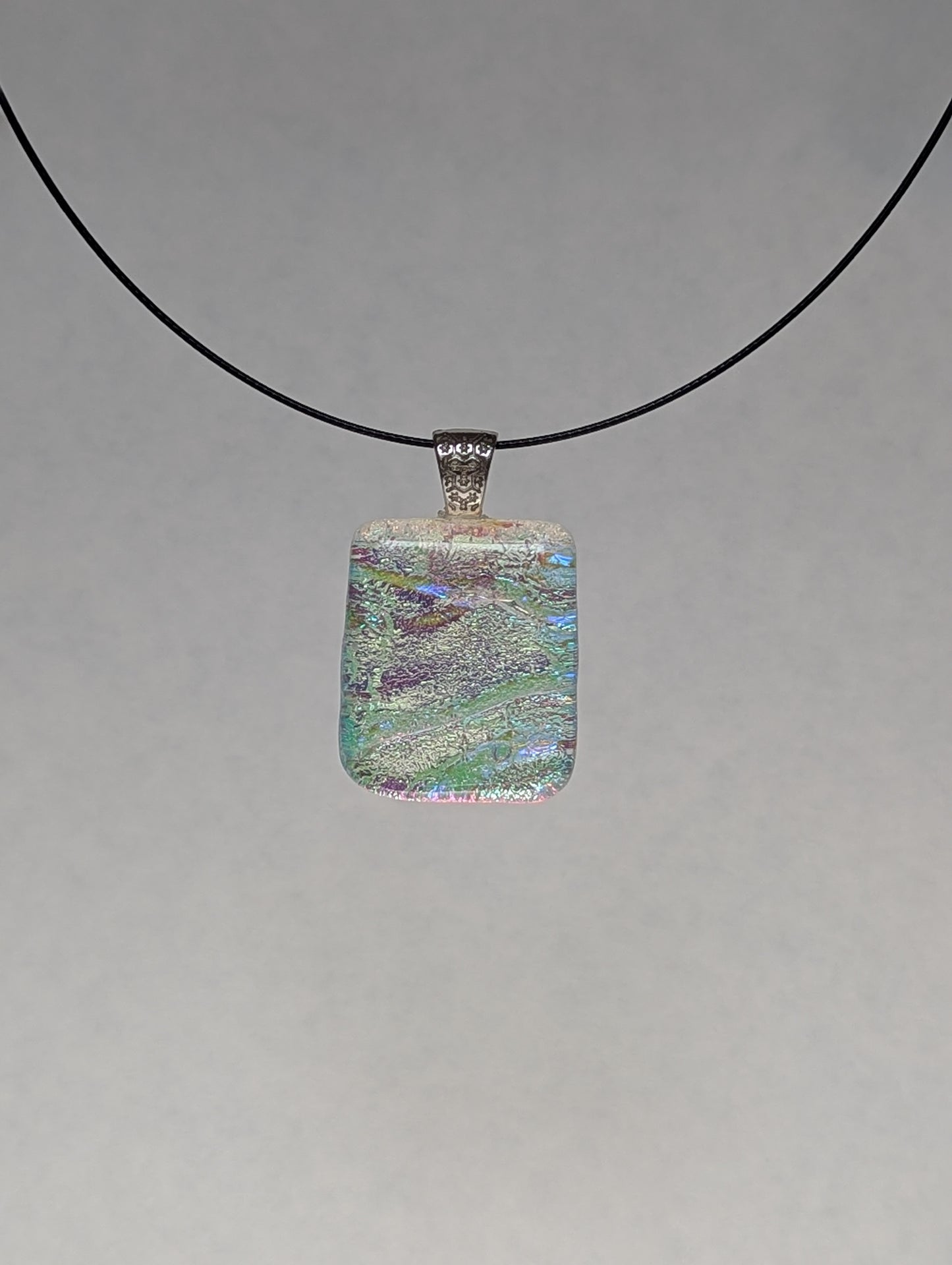 A colorful clear iridescent fused glass pendant with a metallic clasp, displayed on a black stainless steel necklace against a white background.