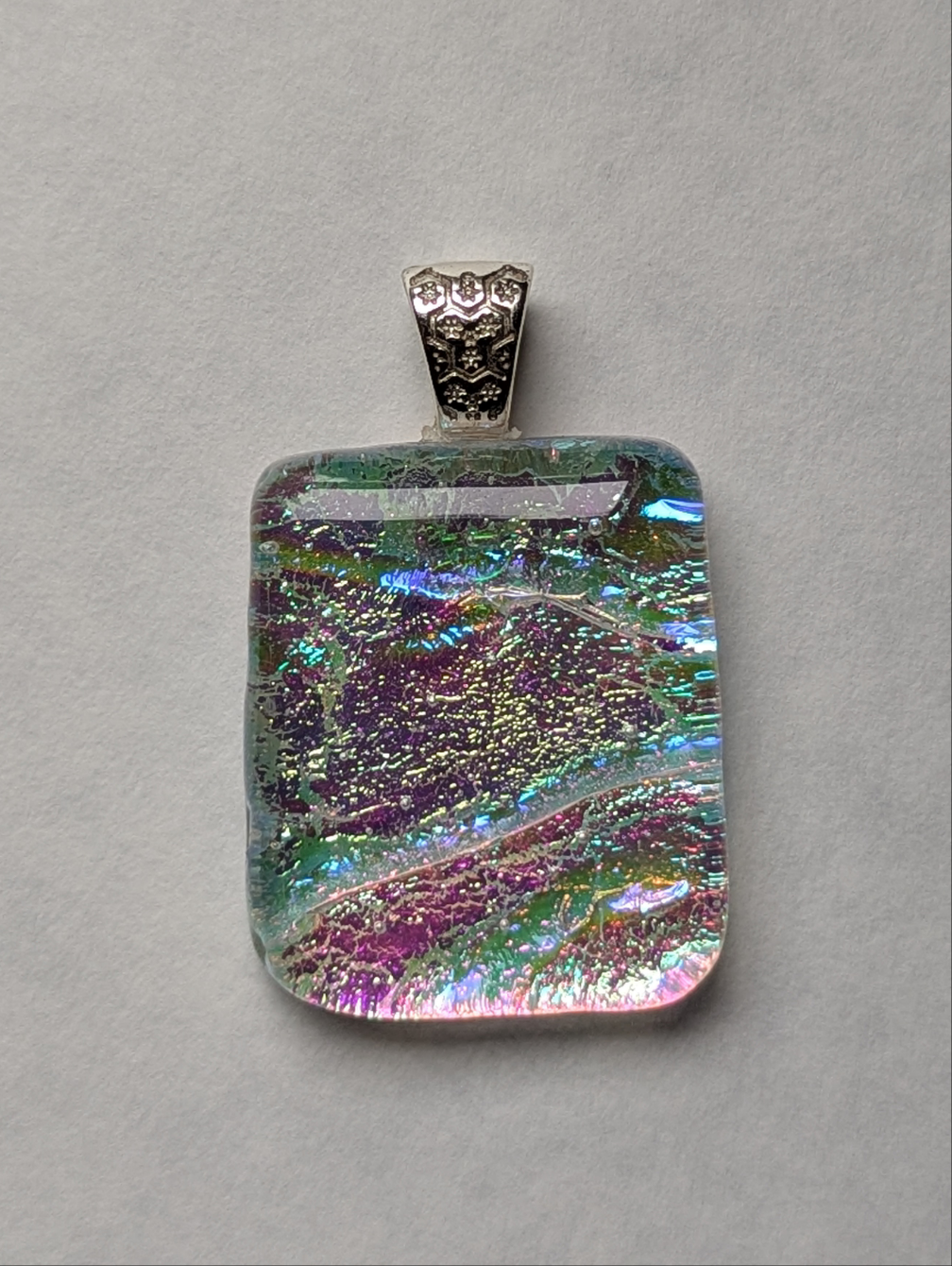 A colorful clear fused glass pendant with a metallic clasp, displaying an eye-catching design.