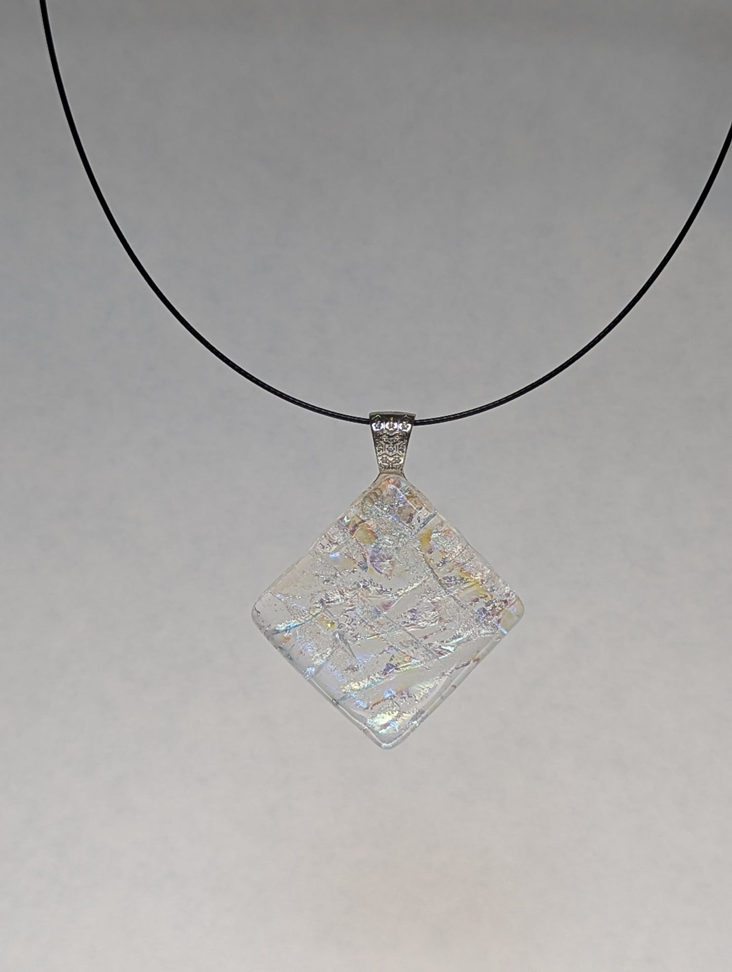 A colorful clear iridescent fused glass pendant with a metallic clasp, displayed on a black stainless steel necklace against a white background.