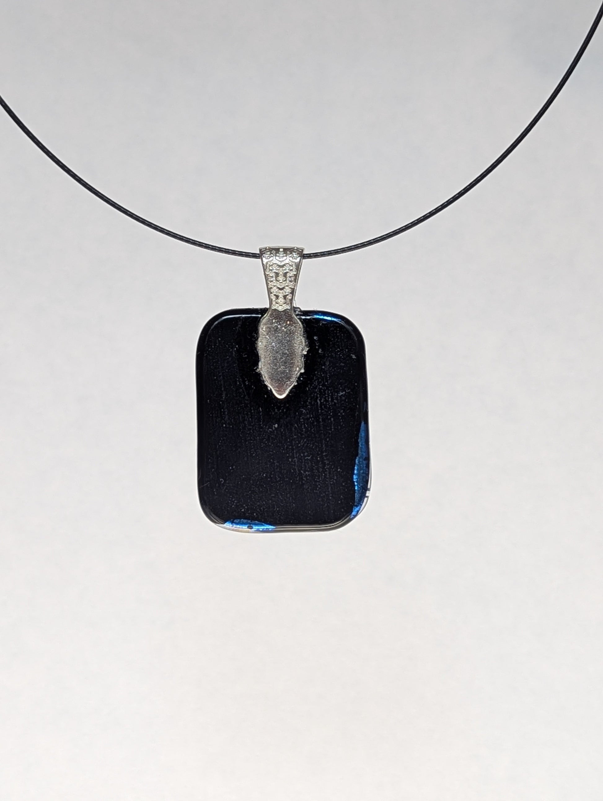 The black back of a blue dichroic fused glass pendant with a silver metallic clasp, displayed on a black stainless steel necklace.