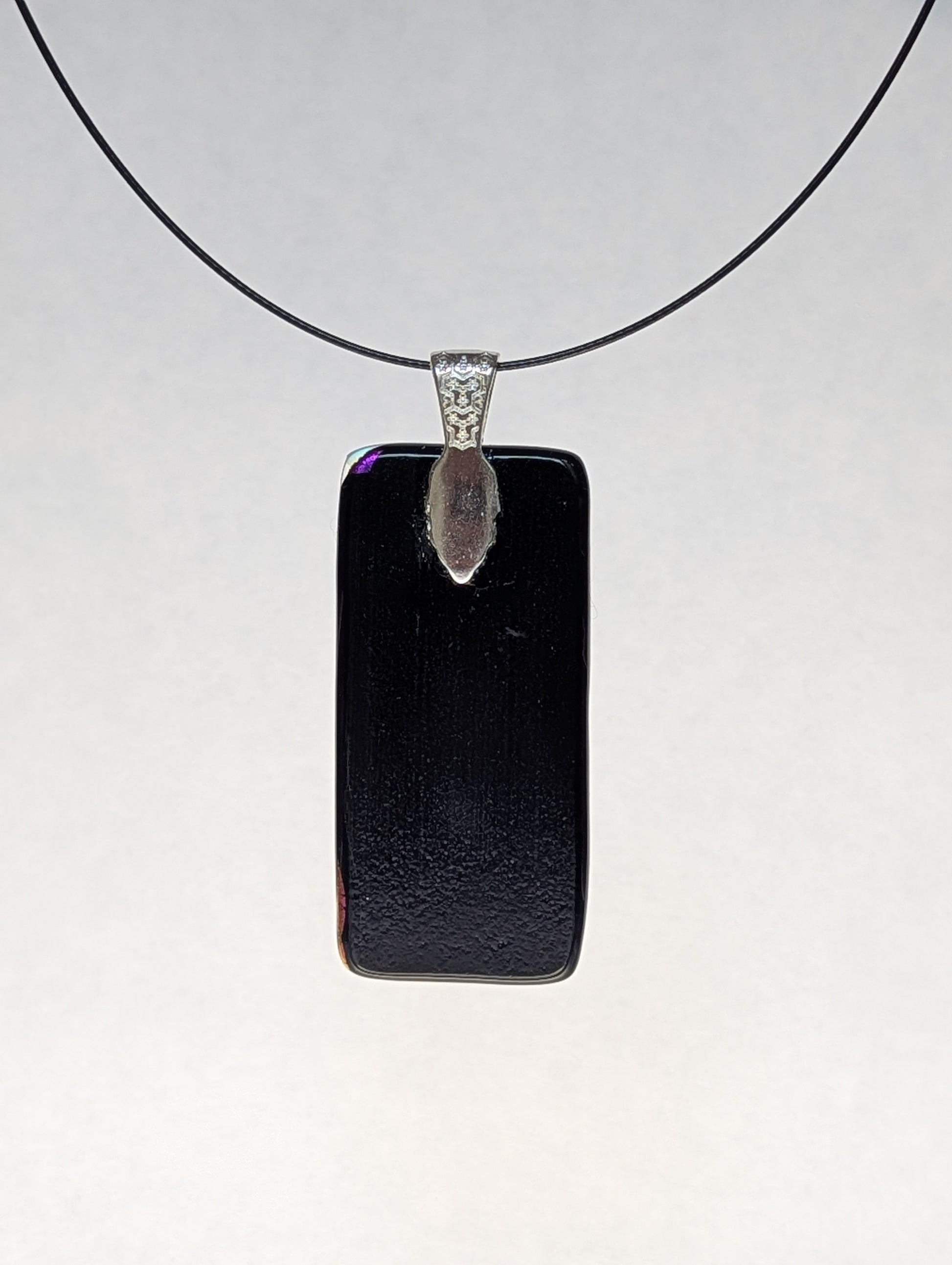 The black back of a purple dichroic fused glass pendant with a silver metallic clasp, displayed on a black stainless steel necklace.