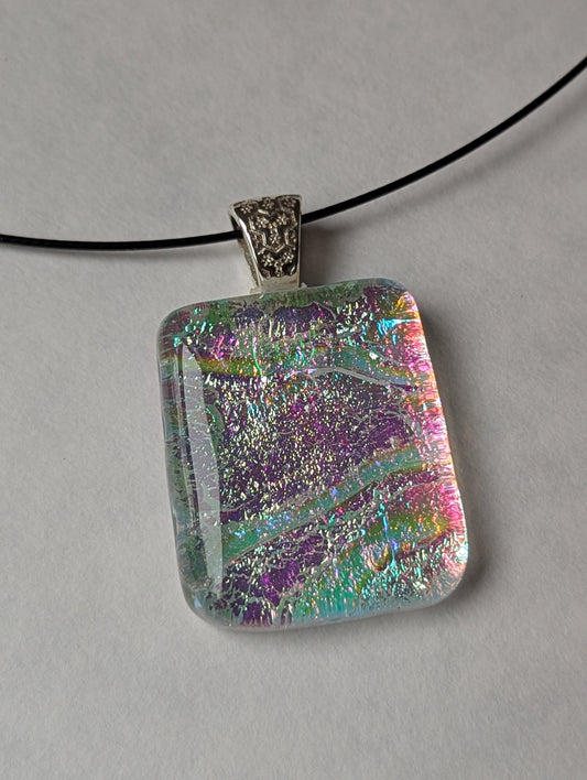 A colorful clear iridescent fused glass pendant with a metallic clasp, displayed on a black stainless steel necklace against a white background.