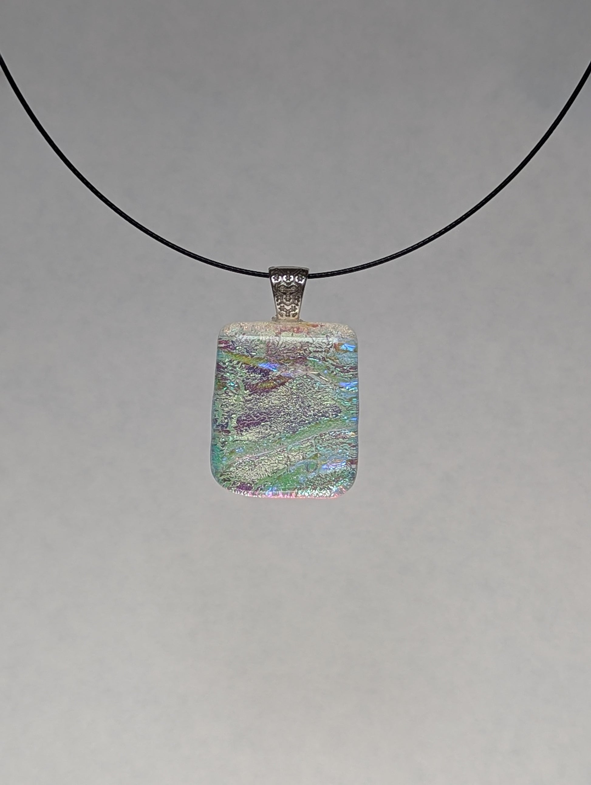 A colorful clear iridescent fused glass pendant with a metallic clasp, displayed on a black stainless steel necklace against a white background.