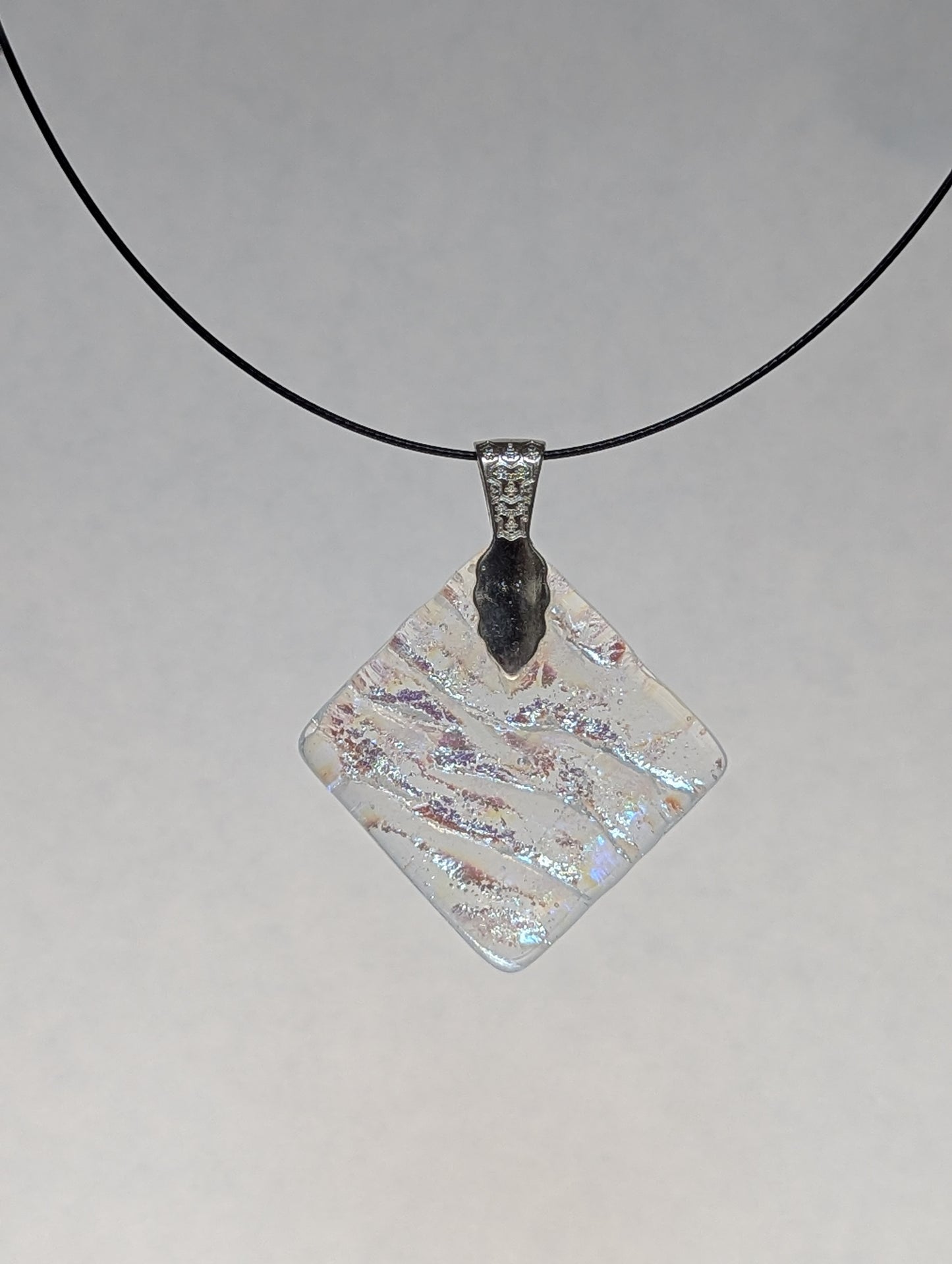 The back of a colorful clear dichroic fused glass pendant with a silver metallic clasp, displayed on a black stainless steel necklace.