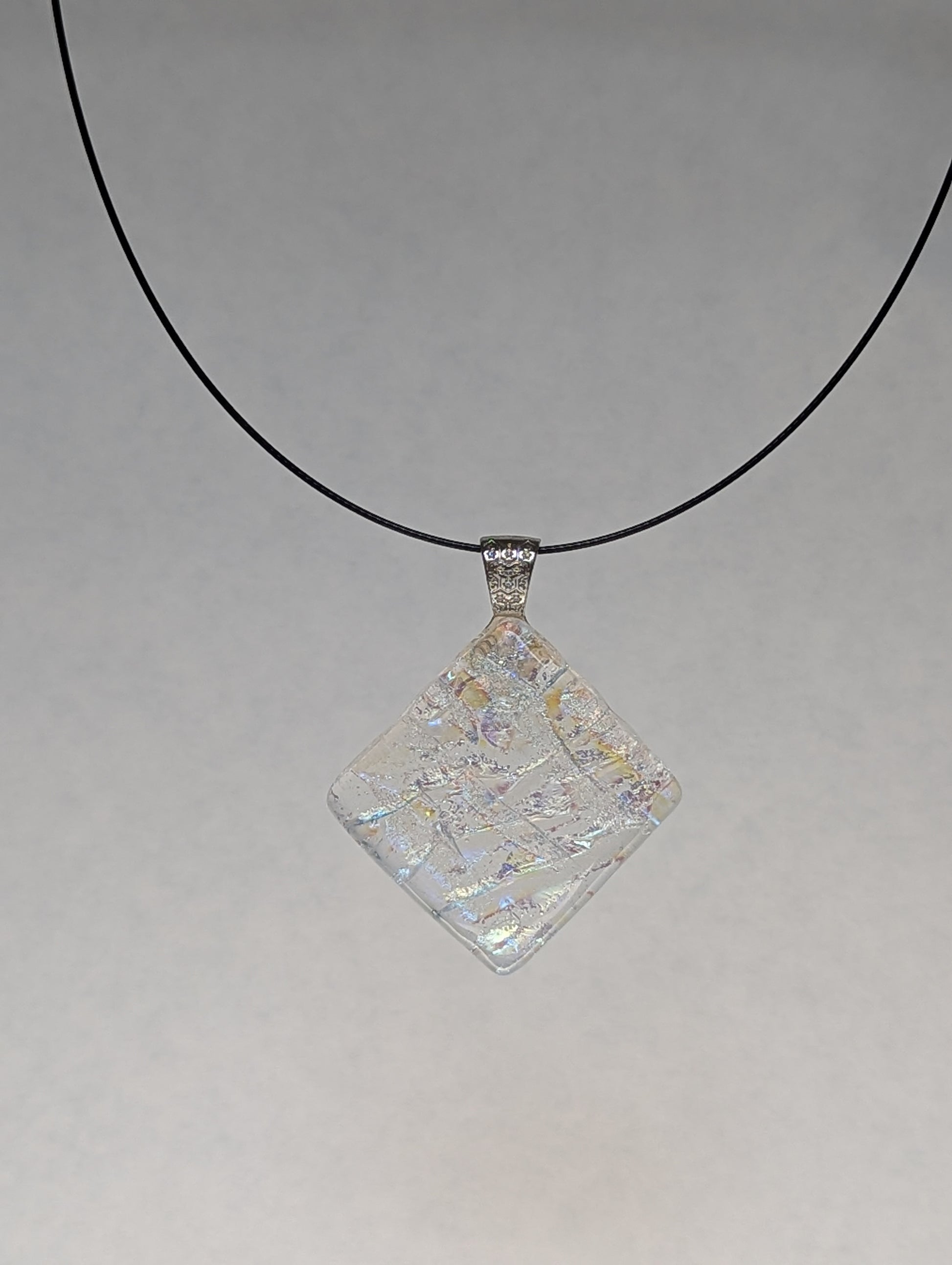 A colorful clear iridescent fused glass pendant with a metallic clasp, displayed on a black stainless steel necklace against a white background.